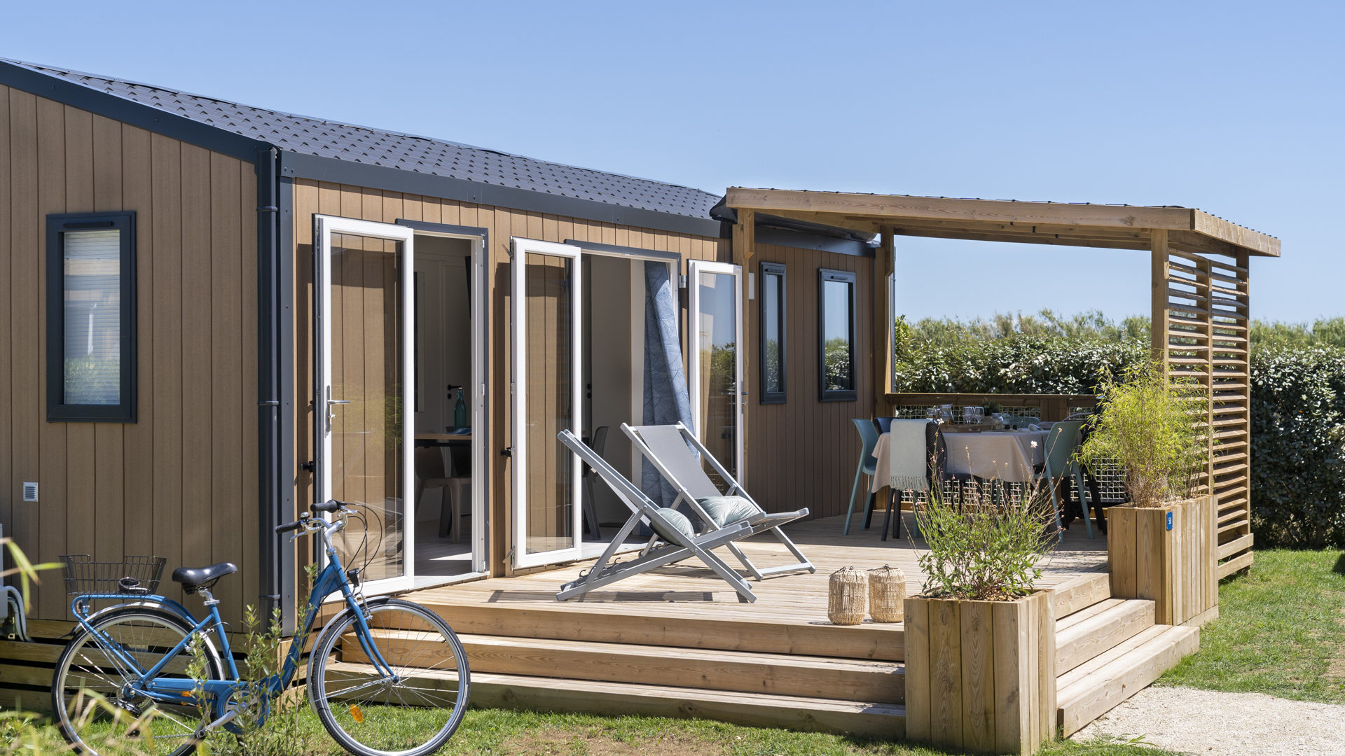 Mobilheim mit Holzterrasse und blauem Fahrrad.